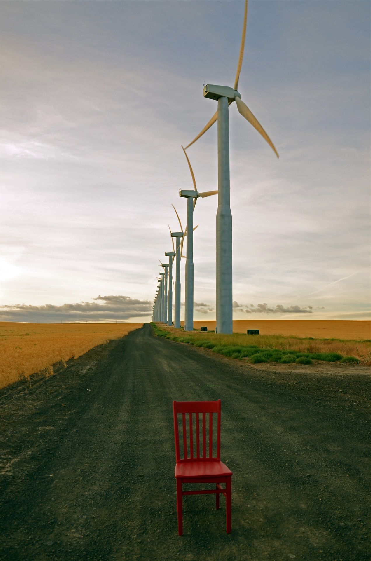 Red chair sitting on a gravel road that is lined with wind turbines