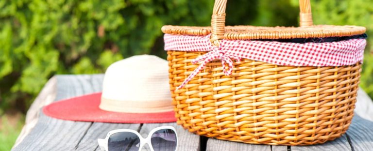 Ready for summer holidays. White sunglasses summer hat and wicker basket on wooden table background. Multicolored vibrant outdoors horizontal image.